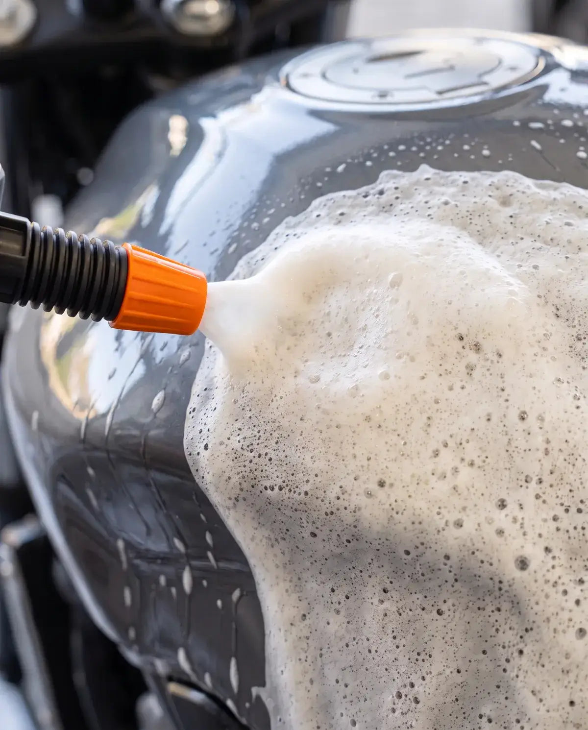 Espuma branca se espalhando sobre o tanque de uma moto, saindo do bico laranja